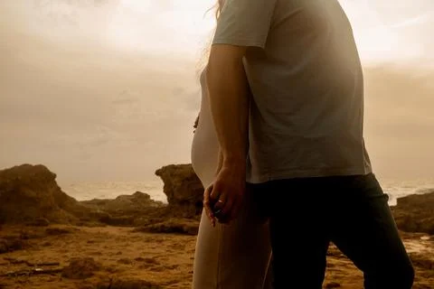 Couple holding hands while standing on rocky shore at sunset near ocean, clou Stock-Fotos