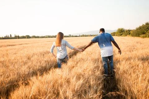 Couple holding hands while walking in field Stock Photos