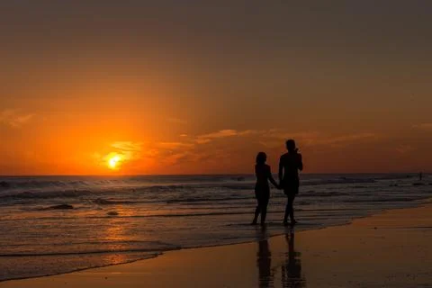 Couple holding hands while walking along the seashore on the beach at sunset. Stock Photos