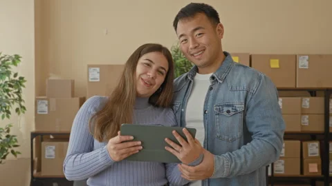 Couple holding tablet and smiling amid packed boxes in a storage building; .. Stock Footage 337445633