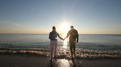 Couple holding their hands going in sea at the sunrise Stock Footage 12273421
