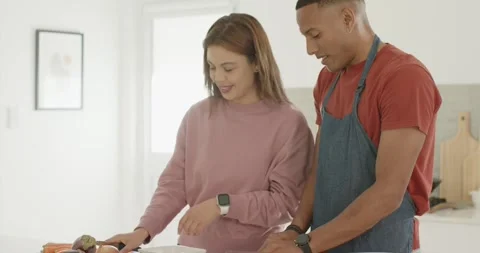 Couple in home kitchen using tablet recipe, man in apron chopping veggies with Stock Footage 344964459
