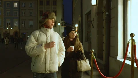 Couple with hot drinks clinking paper cups while walking on a street at night Stock Footage 311462774
