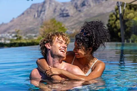 Couple hugging and smiling while looking at each other in infinity pool, Foto stock