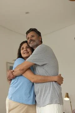 Couple hugging in corner of softly lit living room beside framed wall art and Stock Photos