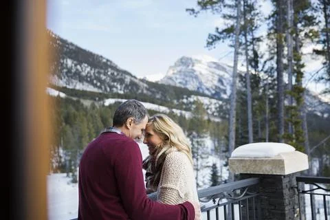 Couple hugging on deck below snowy mountains Stock Photos