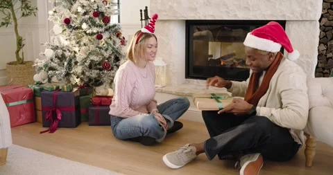Couple hugging man reaching for gift box untying ribbon showing green sweater at Stock Footage 344679263