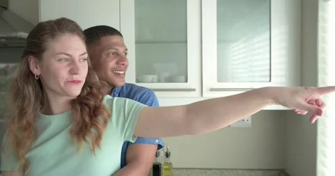 Couple hugging, pointing, looking out kitchen window after spotting view, Stock Footage 337097417
