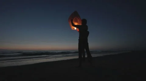 Couple ignites a floating asian lantern at the ocean handheld 2 Stock Footage 40896483