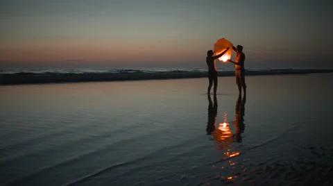 Couple ignites a floating asian lantern at the ocean Stock Footage 41191969