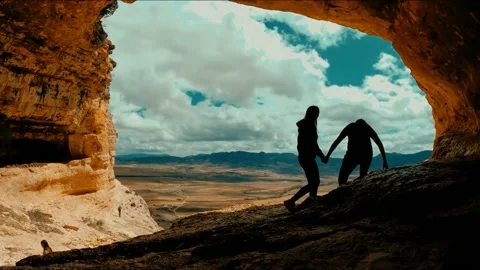 Couple inside cave against landscape. Silhouetted rear view of couple in cavern 스톡 동영상 152793313