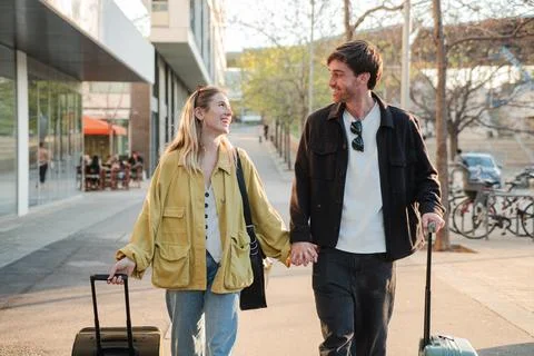 Couple joyfully holding hands while pulling their luggage on a sunny day during Fotos de archivo