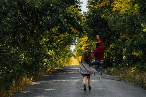 Couple joyfully running down tree lined road Stock Photos