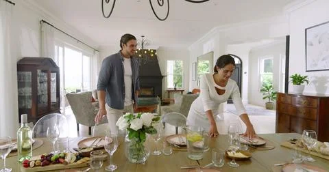 Couple joyfully setting dining table for celebration in elegant living room Stock Photos