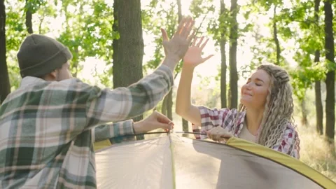 A couple is joyfully setting up a tent together in a beautiful sunlit forest and Stock Footage 280615845