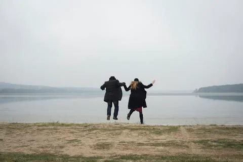Couple jumping while holding hands on a lake shore Foto stock
