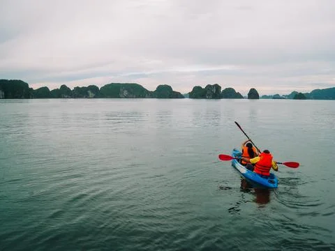 A couple kayaking using paddles going towards the island cave at Halong Bay Stock Photos