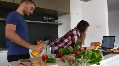 Couple in the kitchen. Man is drinking juice. Women is reading recipe on laptop Stock Footage 61855330