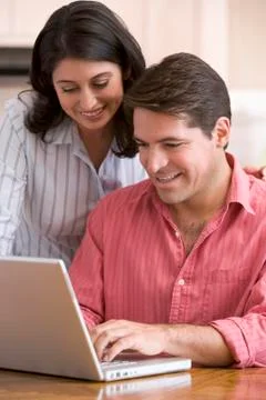 Couple in kitchen with paperwork using laptop smiling Stock Photos