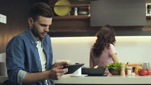 Couple at the kitchen. Smiling man using digital tablet, while woman cooking. Video stock 100076240