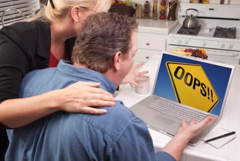 Couple In Kitchen Using Laptop with Yellow Oops Road Sign on the Screen. Stock Photos