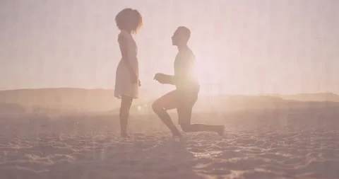 Couple kneeling on beach at sunset, proposing with animated heart icon over ring Stock Footage 308115958