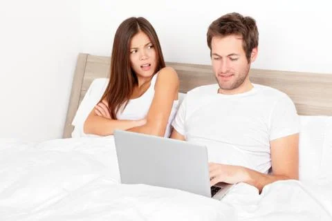 Couple with laptop in bed - Man at computer, woman upset Stock Photos
