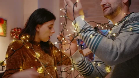 Couple laughing and getting tangled in string of christmas lights Stock Footage 160758925