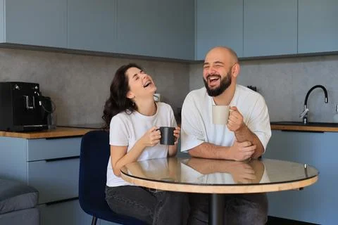 Couple laughing together while drinking coffee in a  kitchen Stock-Fotos