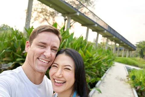 Couple laughing together while taking a selfie in a park during sunset Stock Photos