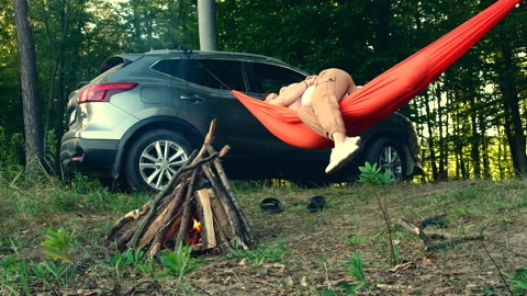 Couple laying in hammock cuddling having fun fireplace in front suv car in ba Stock Footage 213266536