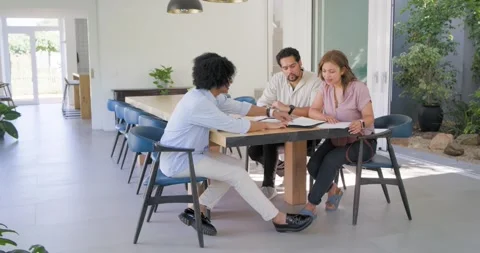 Couple leaning, advisor pointing at binder at dining table at home, man signing Stock-Footage 340969525