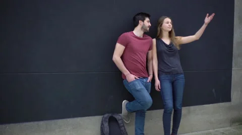 Couple leaning against wall, gesturing and talking about something out of frame Stock Footage 63296662
