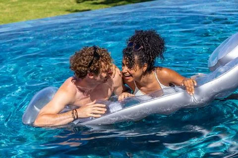 Couple leaning on silver float in clear blue pool, laughing, sunglasses Stock Photos
