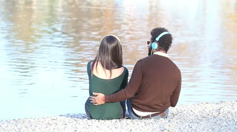 Couple listening to music with headphones, sitting by lake Stock Footage 59555887