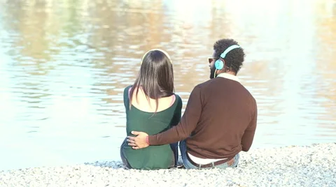 Couple listening to music with headphones, sitting by lake Stock Footage 59555890