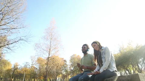 Couple listening to music on headphones while hanging out in park Stock Footage 59554740