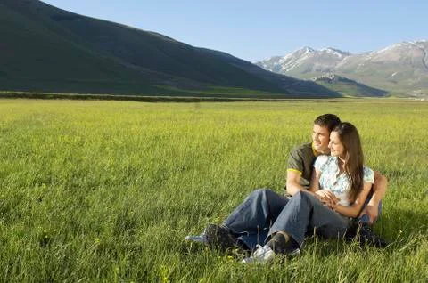 Couple Looking Away While Sitting On Grassy Field Stock Photos