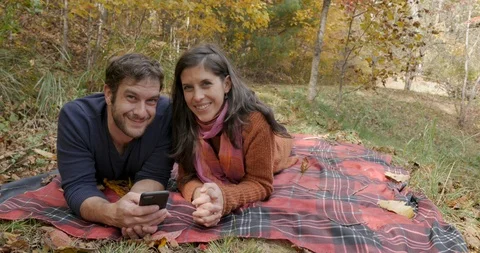 Couple looking at the camera and smiling while lying on a blanket in a park Stock Footage 101445613