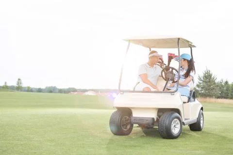 Couple looking at each other while sitting in golf cart against clear sky Fotos Stock