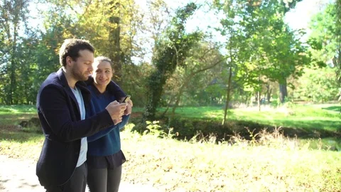 Couple looking at smartphone while strolling through park Stock Footage 75189657