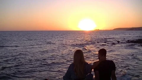 Couple looking at the sunset over the ocean Stockbeeldmateriaal 79605748