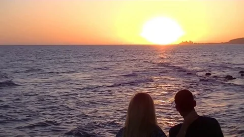 Couple looking at the sunset over the ocean Stockbeeldmateriaal 79605770