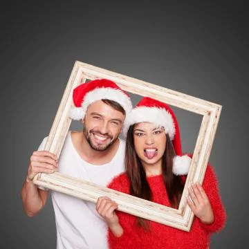Couple looking through frame wearing santa hats Stock Photos