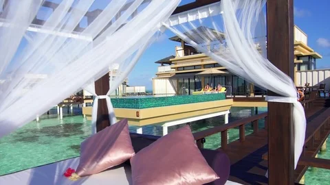 A couple lounges by a pool on an overwater bungalow at a tropical island resort Stock Footage