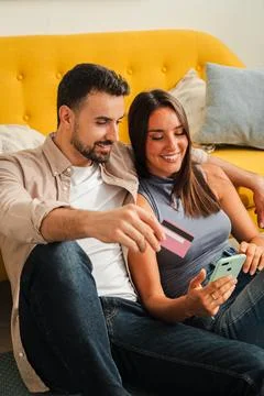 Couple lounging on a bright sofa using smartphone for online purchases with Stock Photos