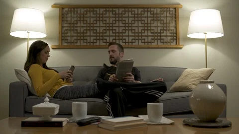 Couple lounging on sofa at home using mobile phone and doing crossword puzzle. Stock Footage 88175969