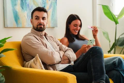 Couple lounging on a yellow sofa using smartphone together, relaxed living room Fotos Stock