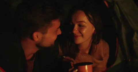 A couple in love drinking coffee lying in their tent near a campfire Stock Footage 264488672