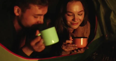 A couple in love drinking coffee lying in their tent near a campfire Stock Footage 264488674